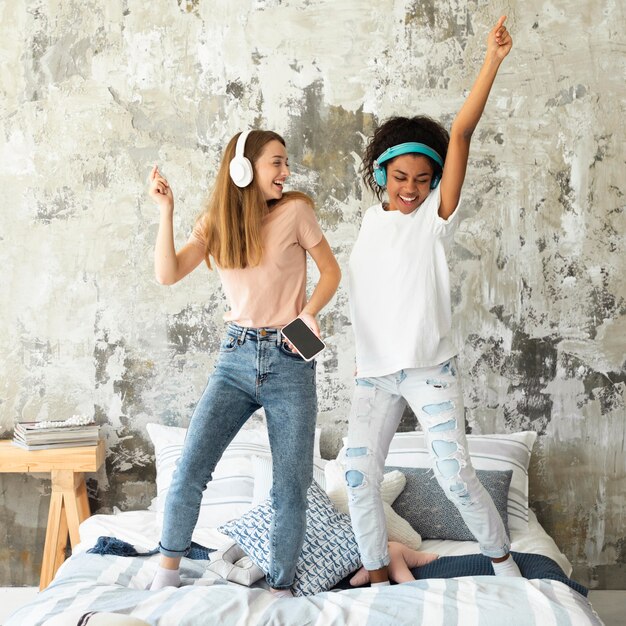 Vriendinnen dansen in bed terwijl u luistert naar muziek op de koptelefoon