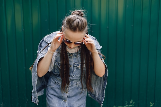 Vrij aantrekkelijk meisje in denim kleding in glazen op een eenvoudige donkergroene achtergrond met lege ruimte voor tekst