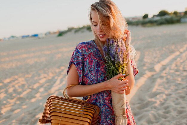 Vrij blonde vrouw die met een boeket van lavendel op het strand loopt. Sunset kleuren.