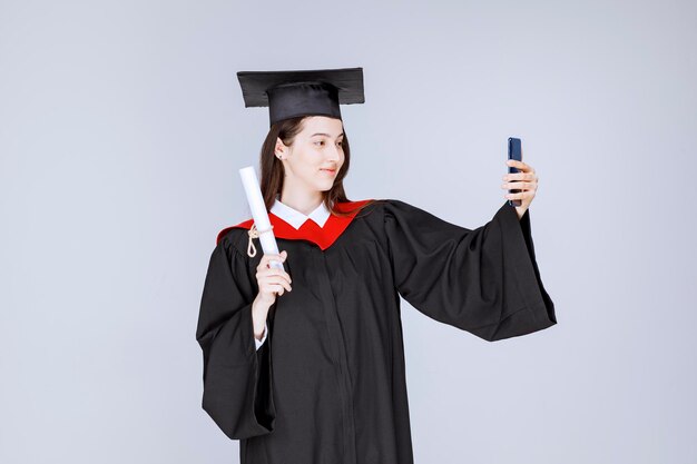 Vrij gediplomeerde student die in toga selfie neemt. Hoge kwaliteit foto