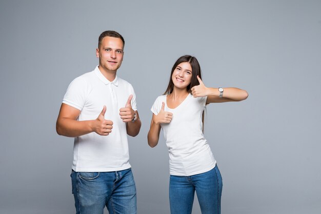 Vrij glimlachend jong paar in vrijetijdskleding thumbs up geïsoleerd op grijs