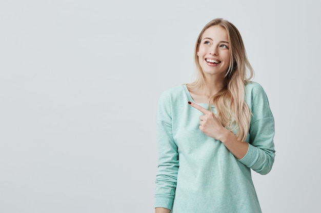 Vrij glimlachend vreugdevolle vrouw met blond haar, wijzend met haar wijsvingers, met kopie ruimte