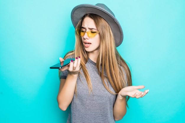 Vrij jong model in maniert-shirt, hoed en transparante bril met telefoon in haar handen die op groene achtergrond wordt geïsoleerd