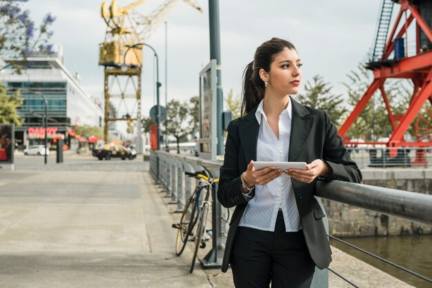 Vrij jonge onderneemster die zich op straat bevindt die mobiel in hand houdt