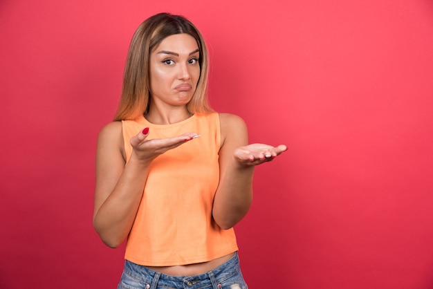 Gratis foto vrij jonge vrouw die verward voorzijde op rode muur kijkt.