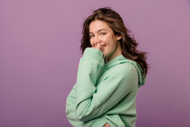 Vrij kaukasische jonge vrouw met donker haar in mint sweatshirt kijkt naar camera op paarse achtergrond leisure lifestyle en beauty concept