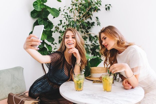 Vrij langharige meisje in elegante jurk selfie met vriend maken tijdens het koelen in een gezellig restaurant