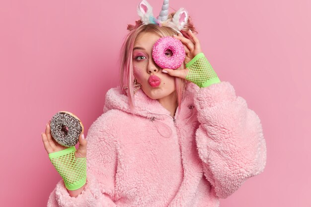 Vrij millennial meisje piuts lippen houdt twee heerlijke zoete donuts geniet van het eten van een dessert