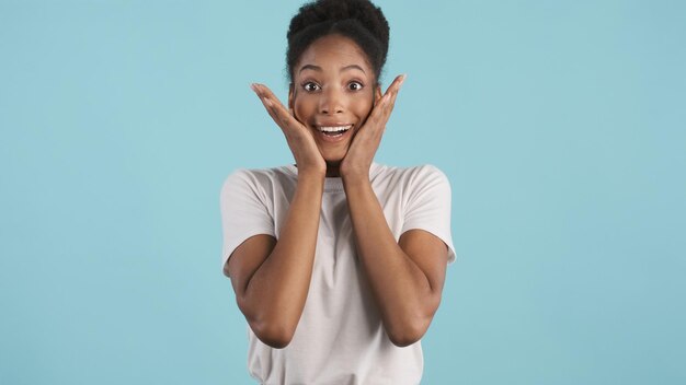 Vrij opgewonden Afrikaans-Amerikaans meisje in wit T-shirt dat verrassend in de camera kijkt over kleurrijke achtergrond Wow-expressie