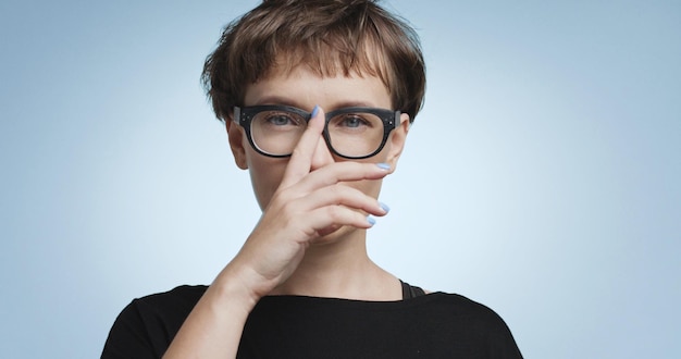 Vrij vrolijke glimlachende jonge vrouw met donker kort haar die een zwarte bovenkant en een bril draagt die op gekleurde achtergronden wordt geïsoleerd