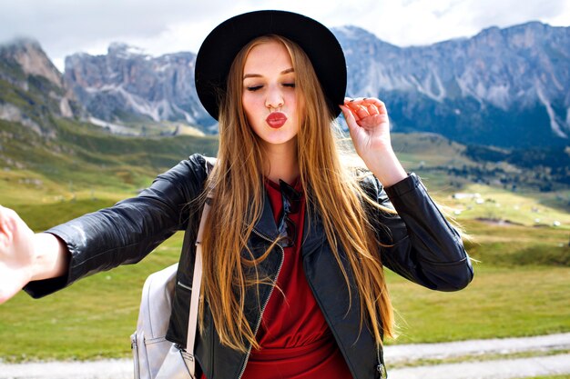 Vrij vrolijke jonge toeristische vrouw stijlvolle leren jas en trendy hoed dragen, selfie maken en haar ogen sluiten