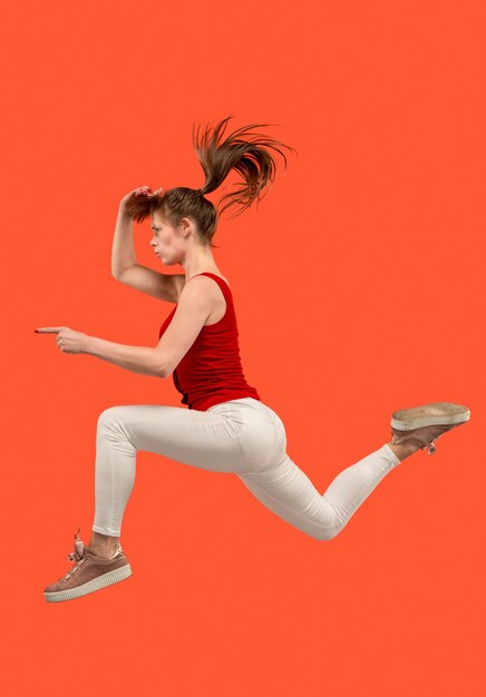 Vrijheid in beweging. In de lucht schot van vrij gelukkige jonge vrouw die en tegen oranje studioachtergrond springt gebaren.