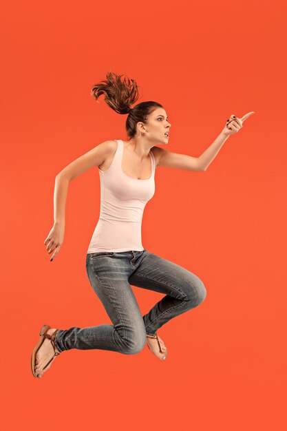 Vrijheid in beweging. In de lucht schot van vrij gelukkige jonge vrouw springen en gebaren tegen oranje studio.