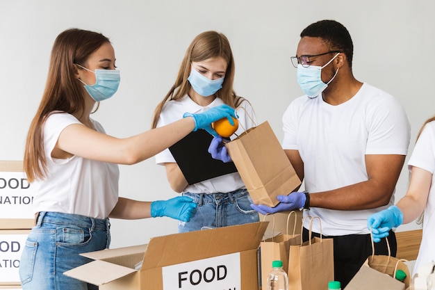 Vrijwilligers met handschoenen en medische maskers die doos met voedsel voorbereiden voor donatie