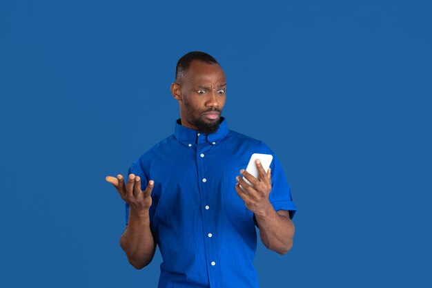 Vroeg me af met behulp van de telefoon. Zwart-wit portret van jonge Afro-Amerikaanse man geïsoleerd op blauwe muur.