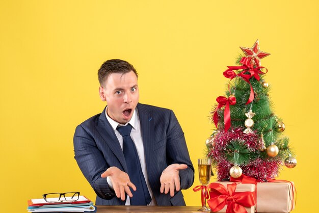 vroeg zich af man zittend aan de tafel in de buurt van kerstboom en cadeautjes op geel