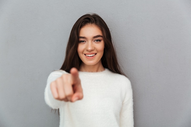 Vrolijk aantrekkelijk meisje in witte pluizige pullover wijzend met de vinger op je