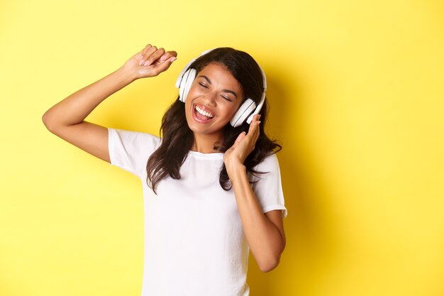Vrolijk Afro-Amerikaans tienermeisje dat naar muziek luistert in een koptelefoon die vrolijk danst en zingt