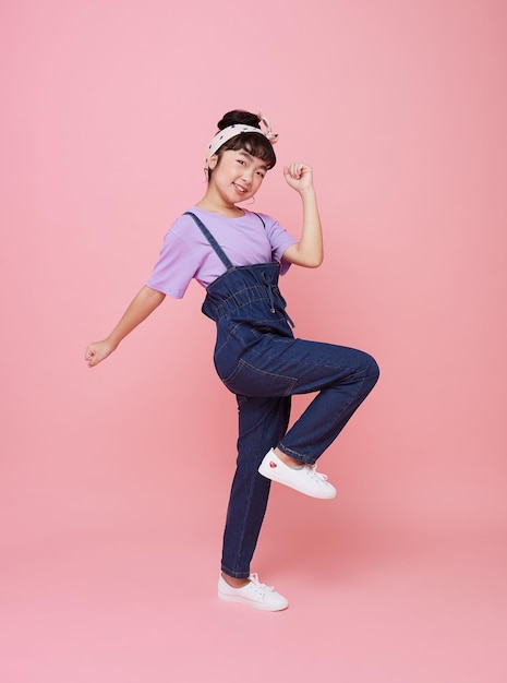 Vrolijk Aziatisch kindmeisje viert feest met opgeheven vuisten kijkend naar camera geïsoleerd op roze achtergrond