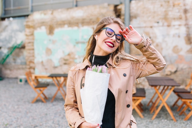 Gratis foto vrolijk blij meisje met paarse tulpen kwam na een drukke dag naar het café. mooie jonge vrouw die haar verjaardag viert op het terras heeft een boeket bloemen gekregen als een geschenk. dating bij restaurant