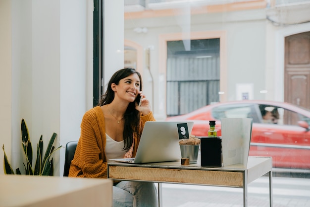 Gratis foto vrolijk brunette die op telefoon in koffie spreken