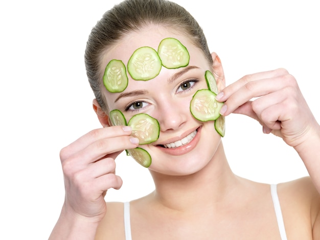 Vrolijk gelukkig mooi meisje gezichtsmasker van komkommer geïsoleerd op wit toe te passen