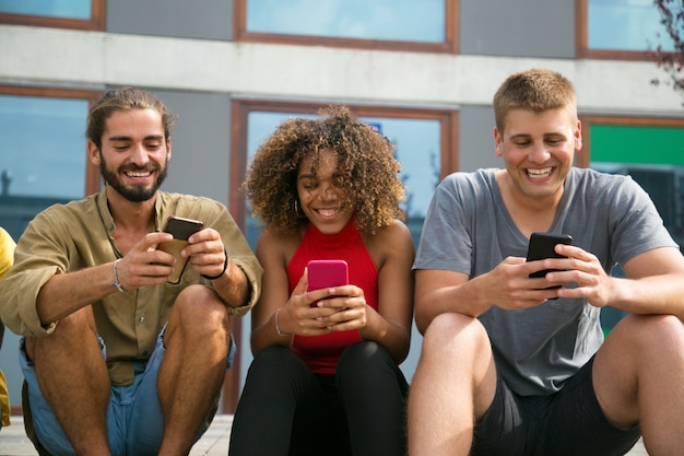 Vrolijk gerichte multi-etnische studenten die hun telefoons gebruiken