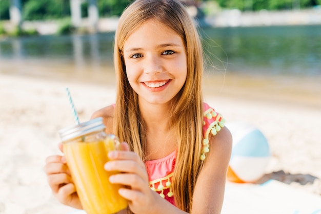 Gratis foto vrolijk glimlachend meisje met drank op kust