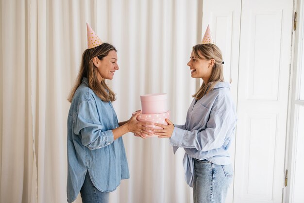 Vrolijk jong meisje met een lichte huid feliciteert haar blonde oudere zus bij een speciale gelegenheid in de buurt van een witte achtergrond. Concept van feest, geluk en emoties.