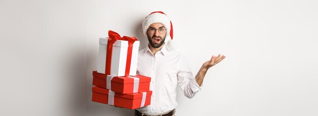 Vrolijk kerstfeest concept man die verward kijkt terwijl hij kerstcadeaus vasthoudt en verbaasde sta