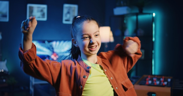 Gratis foto vrolijk kind dat haar volgers betovert met ongelooflijke dansbewegingen in een neonverlichte thuisstudio