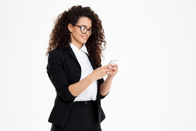 vrolijk krullend bedrijfsmeisje dat glazen draagt die telefoon bekijken