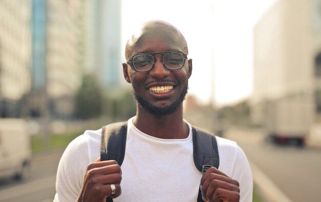 Vrolijk lachend Afrikaans mannetje met een bril met een wit t-shirt en een rugzak op straat