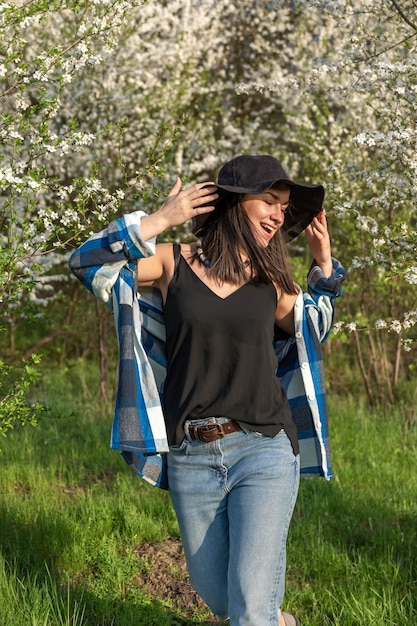 Vrolijk meisje in een hoed tussen de bloeiende bomen in de lente, in een casual stijl