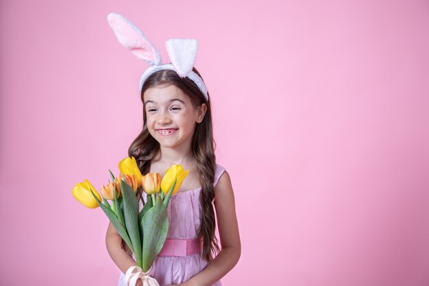Vrolijk meisje met paashaas oren glimlacht en houdt een boeket tulpen in haar handen op een roze studio achtergrond