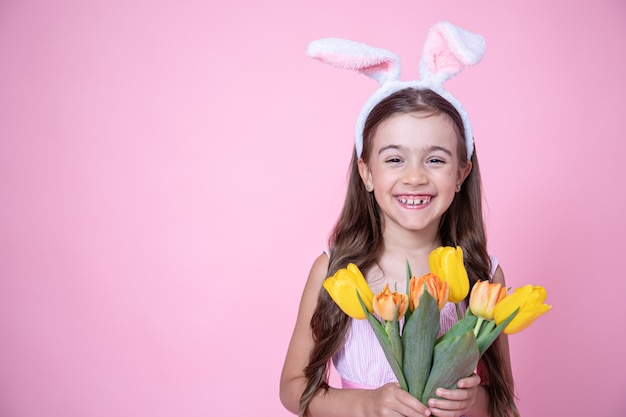 Vrolijk meisje met paashaas oren glimlacht en houdt een boeket tulpen in haar handen op een roze studio