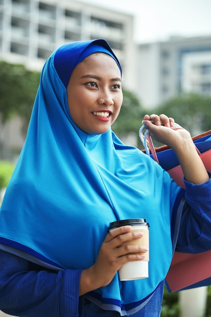 Vrolijk moslimvrouwtje met warme drank na het winkelen