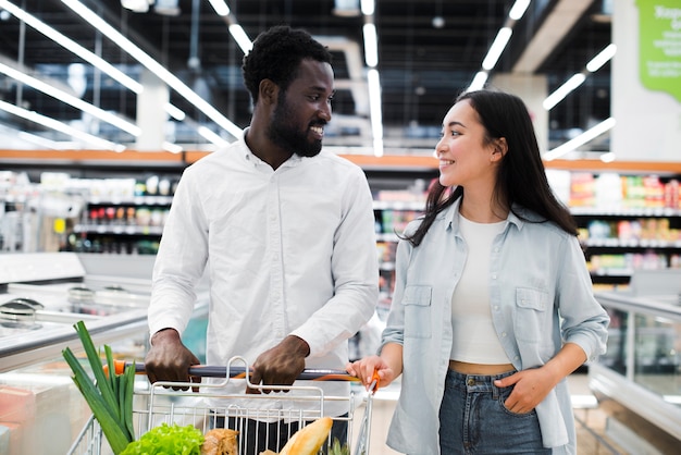 Vrolijk multiraciaal paar met boodschappenwagentje bij supermarkt