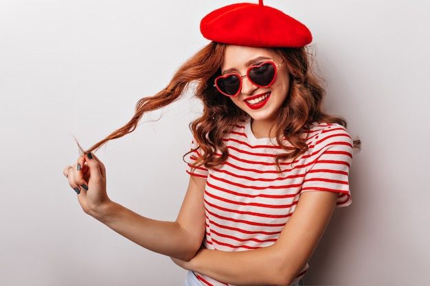 Vrolijk roodharig meisje dat haar krullend haar speelt. extatische knappe vrouw in baret.