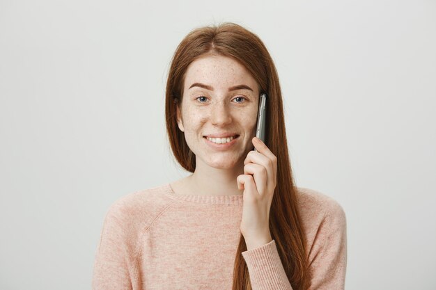 Vrolijk roodharig meisje met sproeten, glimlachend en zorgeloos aan de telefoon praten