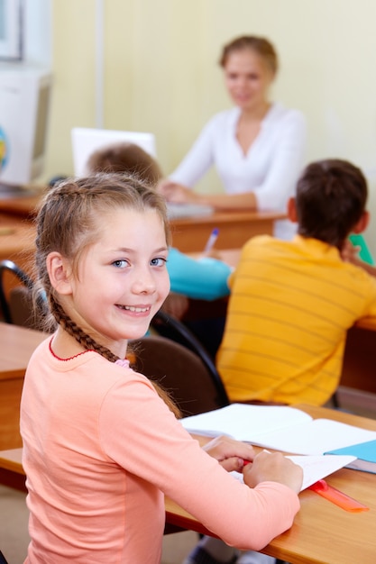 Vrolijk schoolmeisje bij haar bureau in de klas