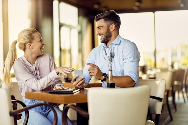 Vrolijk stel dat plezier heeft tijdens het gebruik van een smartphone in een café