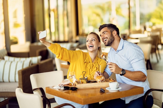 Vrolijk stel dat selfie met mobiele telefoon neemt tijdens het eten in een restaurant