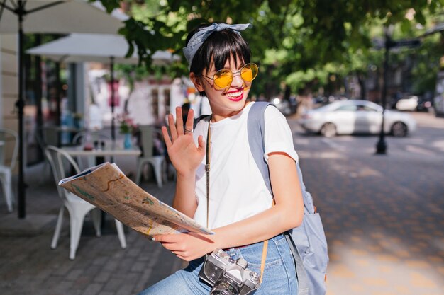 Vrolijk trendy meisje met zwaaiende hand in zilveren ring en glimlachen, wegkijken