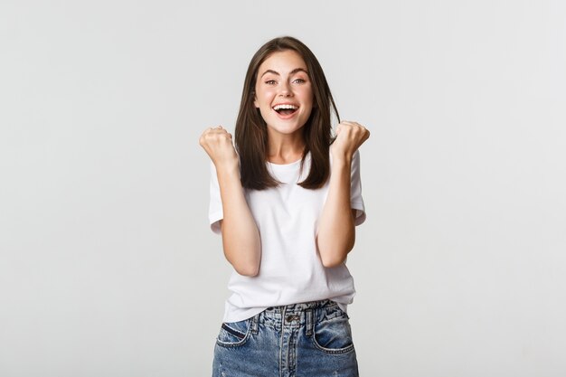 Vrolijke aantrekkelijke brunette meisje vuist pomp en lachend met vreugde, winnen