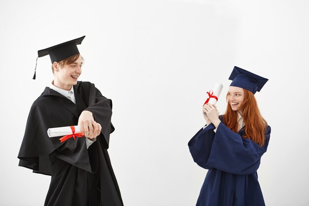 Vrolijke afgestudeerden glimlachend vechten met diploma's.