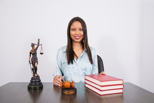 Vrolijke Afrikaanse Amerikaanse vrouw aan tafel met hamer, boeken en standbeeld
