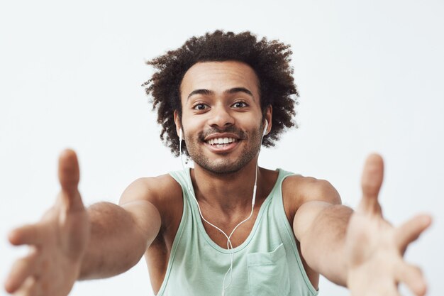 Vrolijke Afrikaanse mens die in bedrade hoofdtelefoons uitrekkende handen glimlachen die uw celtelefoon proberen te stelen.