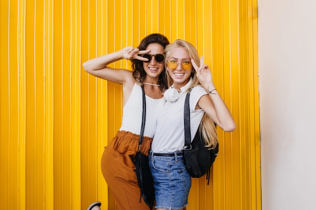 Vrolijke blonde vrouw in gele zonnebril gek rond met beste vriend.