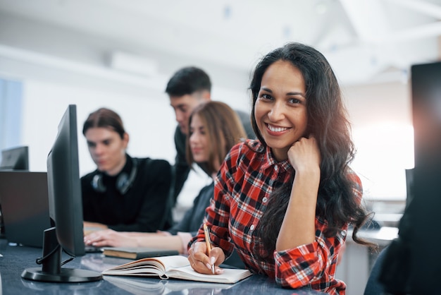 Vrolijke brunette. Groep jonge mensen in vrijetijdskleding die in het moderne bureau werken